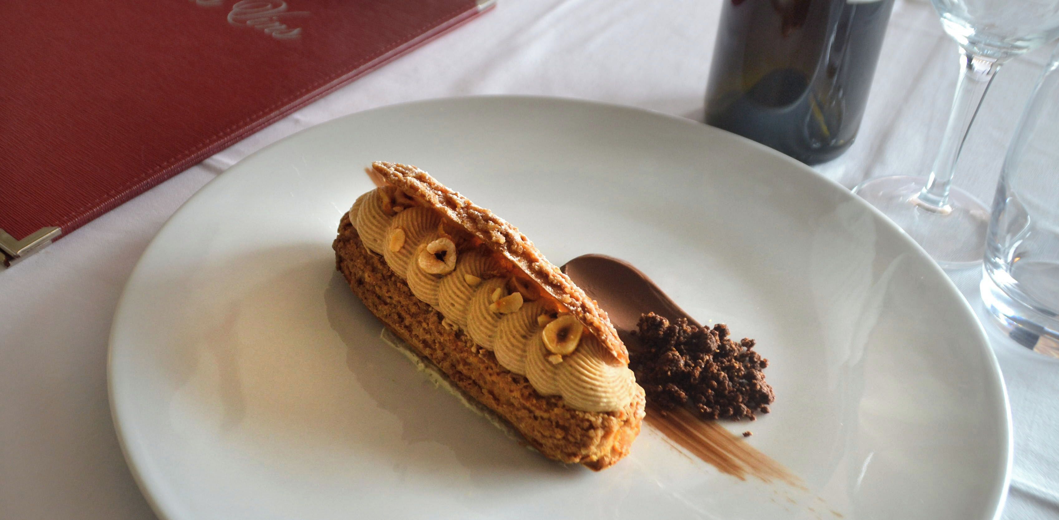 A dessert on a white plate with a spoon, a red menu, and a glass of water on a table.