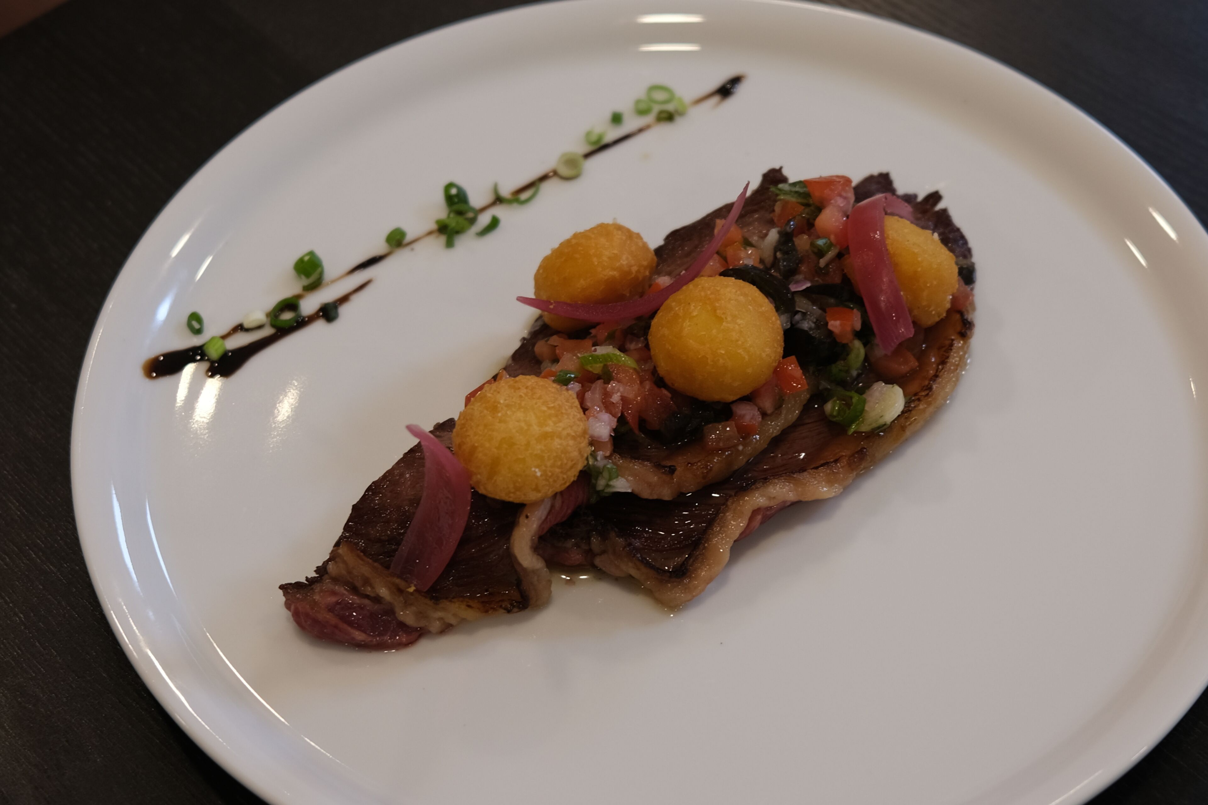Une assiette blanche contenant un morceau de viande, garni de légumes et nappé de sauce.