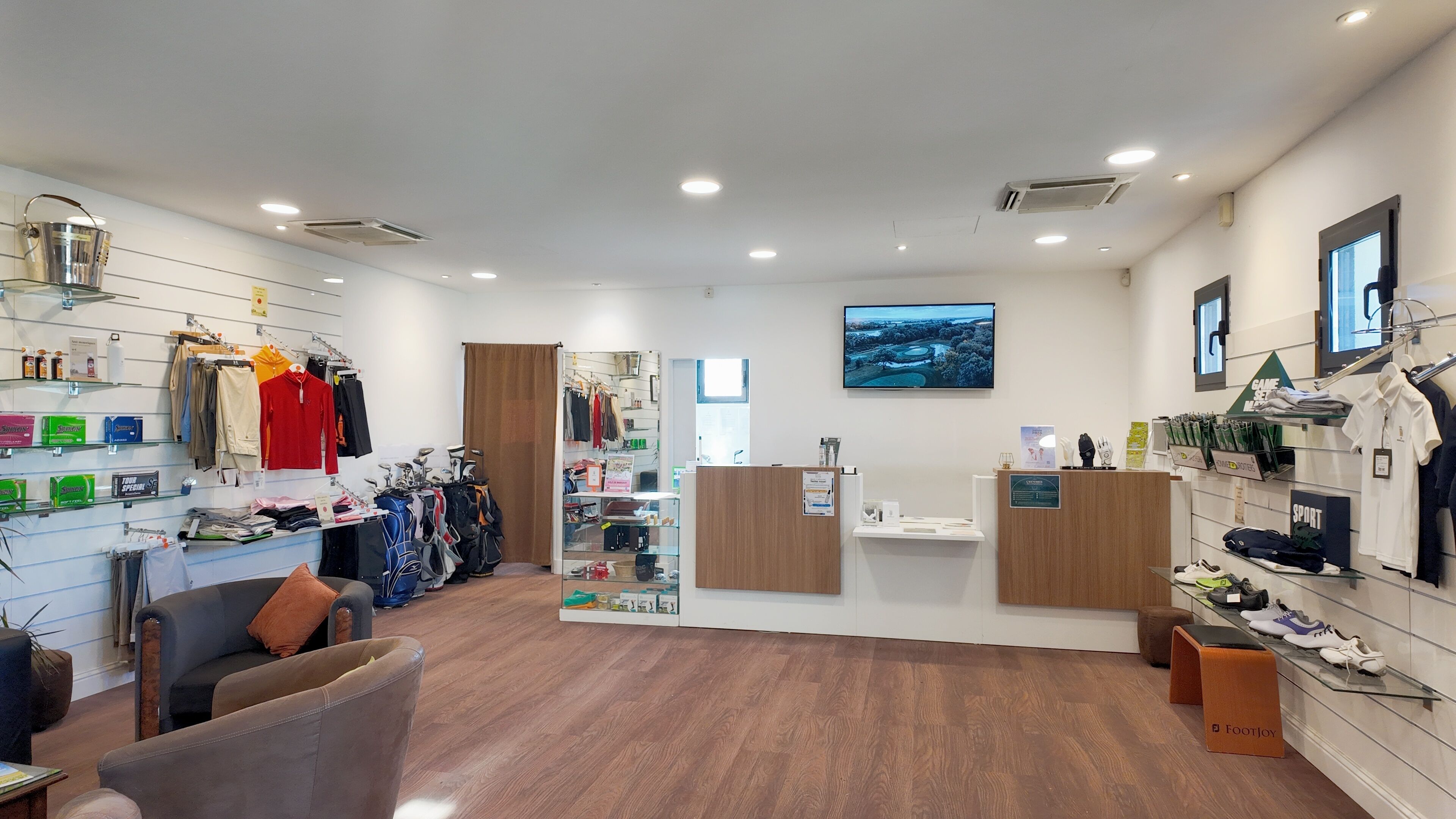 Una tienda moderna con percheros de ropa, un mostrador de recepción y una exhibición de bolsas de golf.