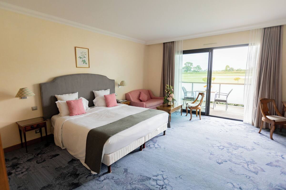 Une chambre d’hôtel avec un grand lit, un petit bureau, une chaise et un balcon donnant sur l’extérieur.