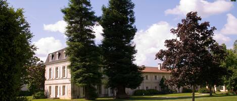 A large building with a symmetrical facade, surrounded by a well-maintained lawn and several tall trees.