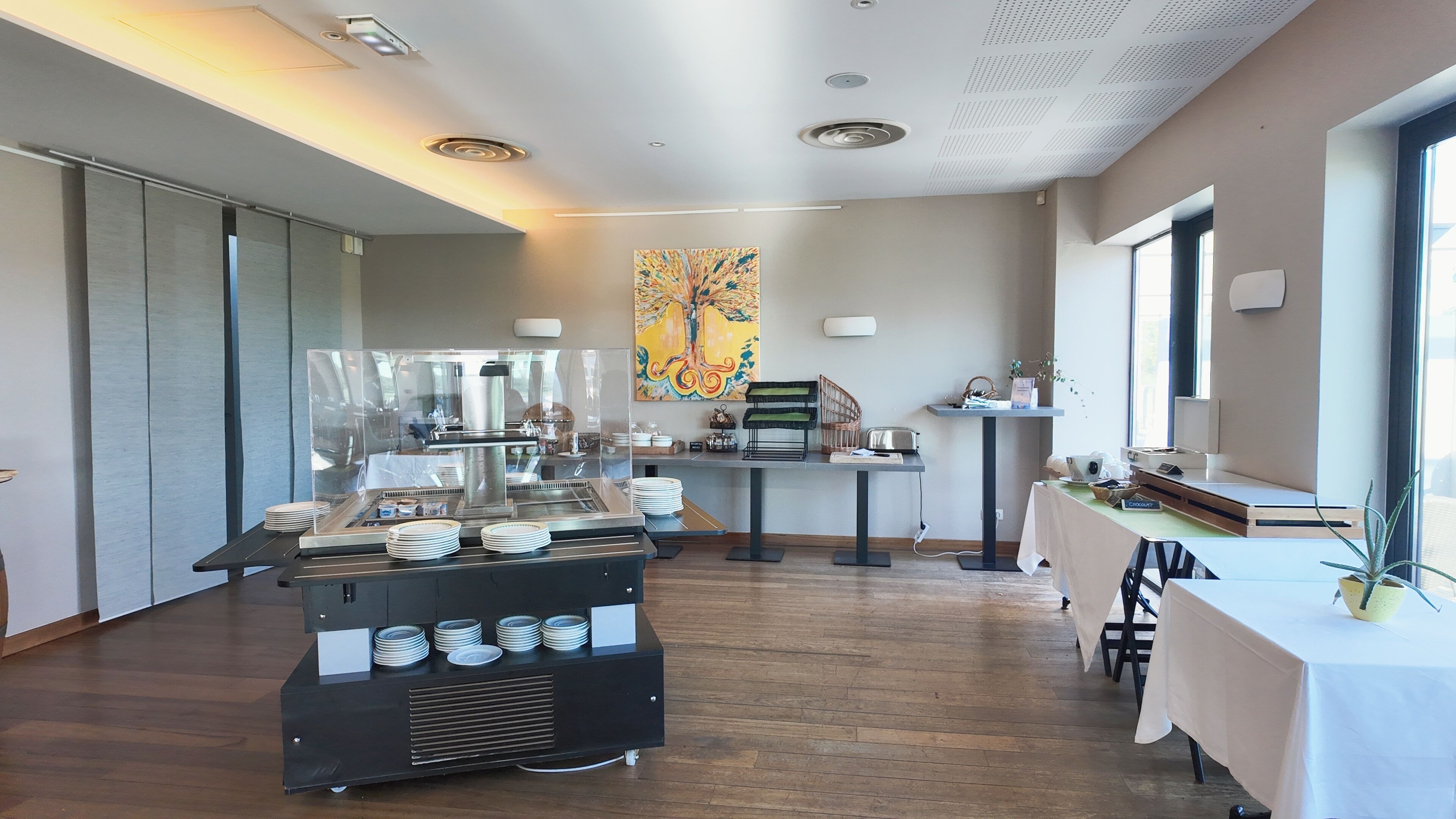 A modern dining area with a buffet setup, a large abstract painting on the wall, and a window providing natural light.