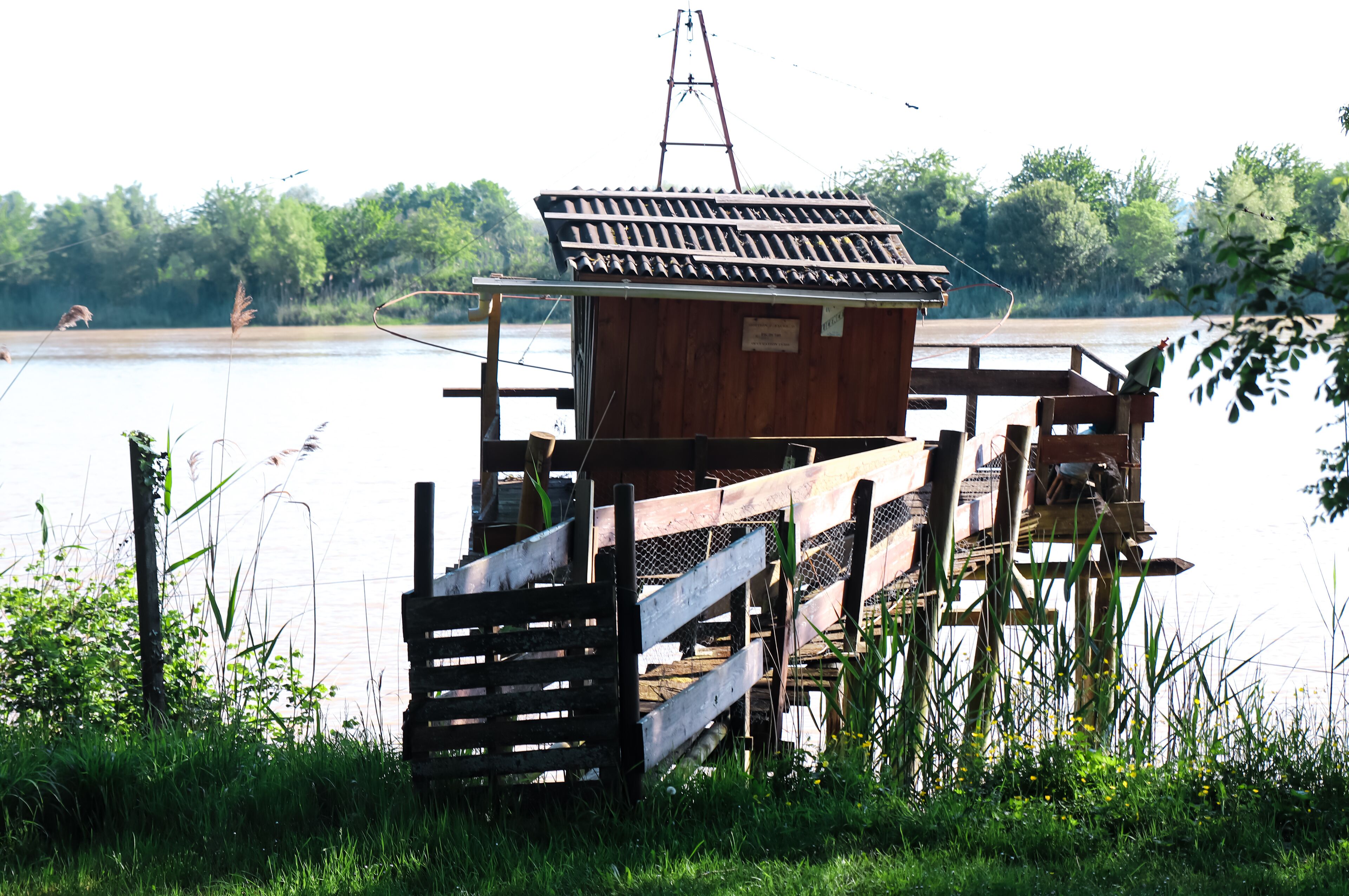 A wooden dock with a small cabin, surrounded by water and greenery.