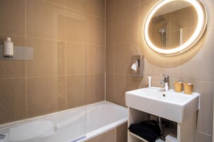 Ein modernes Badezimmer mit einer Badewanne, einem Waschbecken mit zwei Tassen und einem Spiegel mit Beleuchtung.