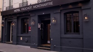 A hotel facade with a sign reading 'HOTEL FROCHOT MONTMARTRE,' featuring a classic architectural style with multiple windows and balconies.