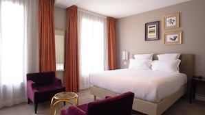 A hotel room with a bed, two chairs, a small table, and a nightstand.