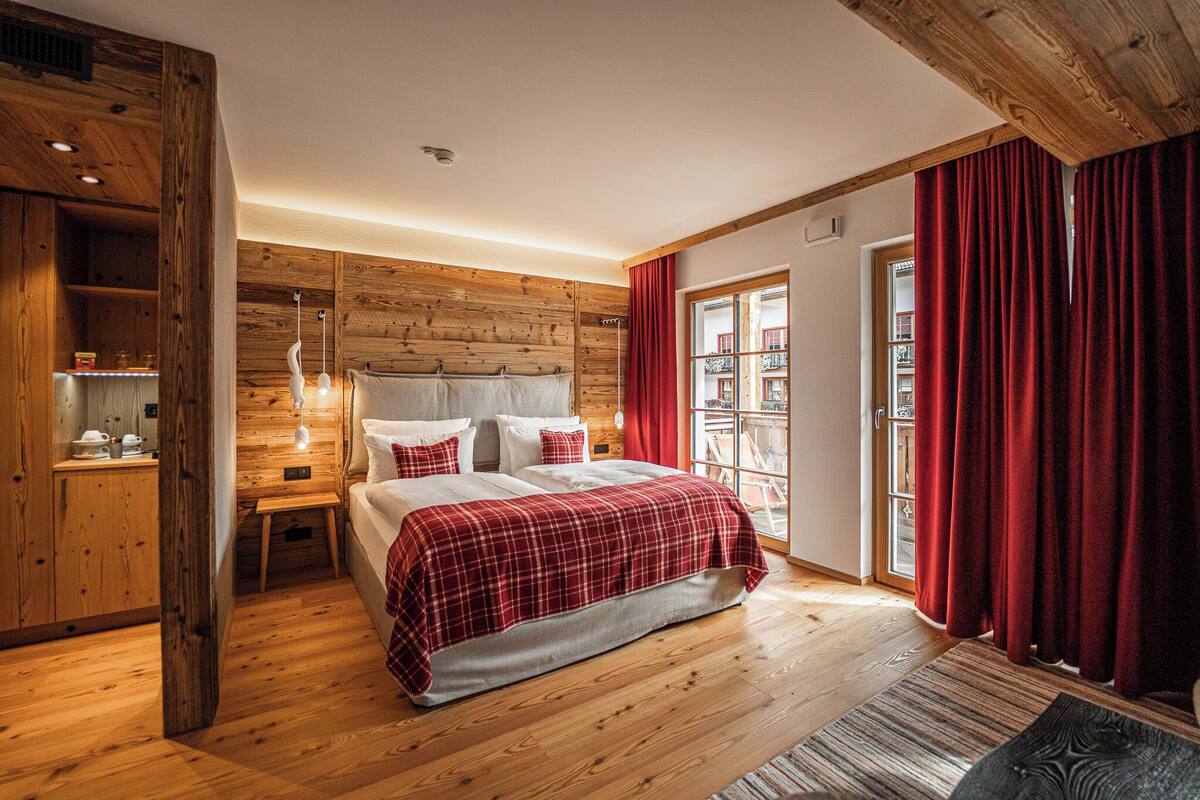 A wooden-paneled bedroom with a bed, a nightstand, and a window with red curtains.