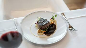 A plate with a steak, sauce, and garnish on a white tablecloth.