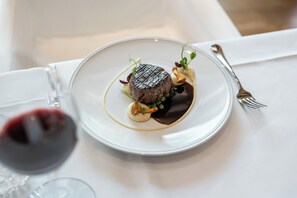 A plate with a steak, sauce, and garnish on a white tablecloth.
