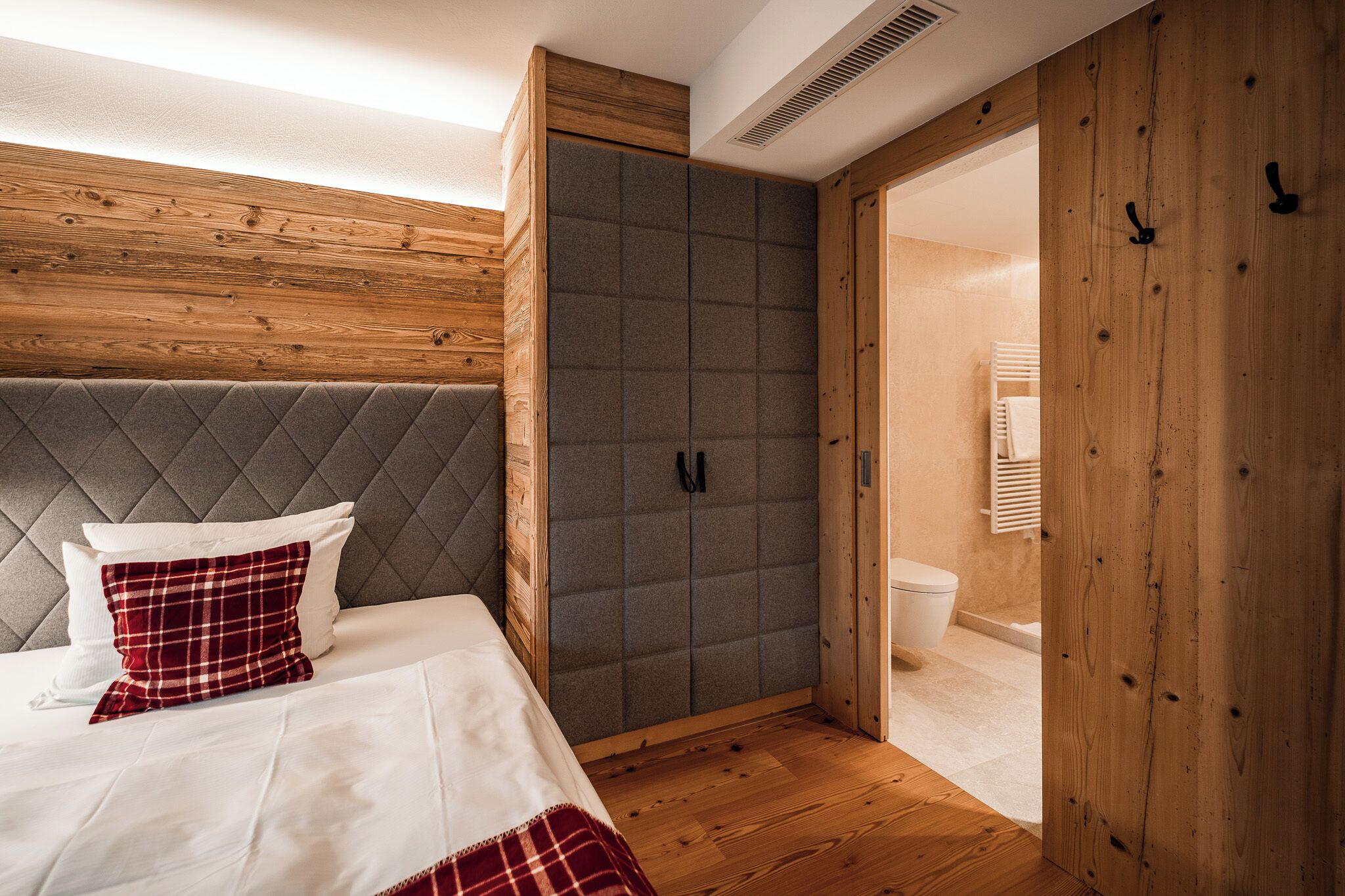 Un dormitorio con una cama, un armario tapizado en gris, paredes de madera y suelo de madera.