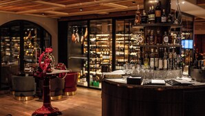 A bar area with a wine rack, bar stools, and a large ice bucket. - Resort Das Achental (Grassau)