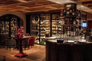 A bar area with a wine rack, bar stools, and a large ice bucket. - Resort Das Achental (Grassau)