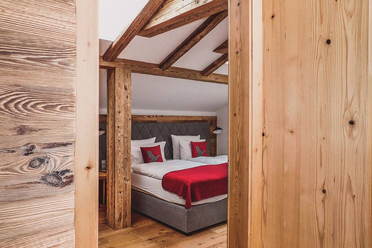 A bedroom with a wooden ceiling, a bed with red bedding, and a grey headboard.