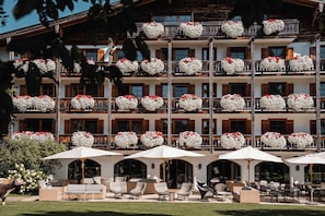 A multi-story hotel with balconies adorned with flower arrangements, outdoor seating with umbrellas, and a well-maintained lawn.