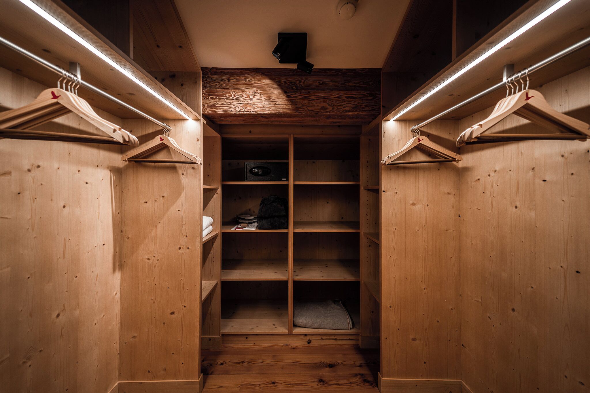 Un placard en bois, doté d’étagères et d’une tringle pour suspendre les vêtements, éclairé par un éclairage installé au plafond.