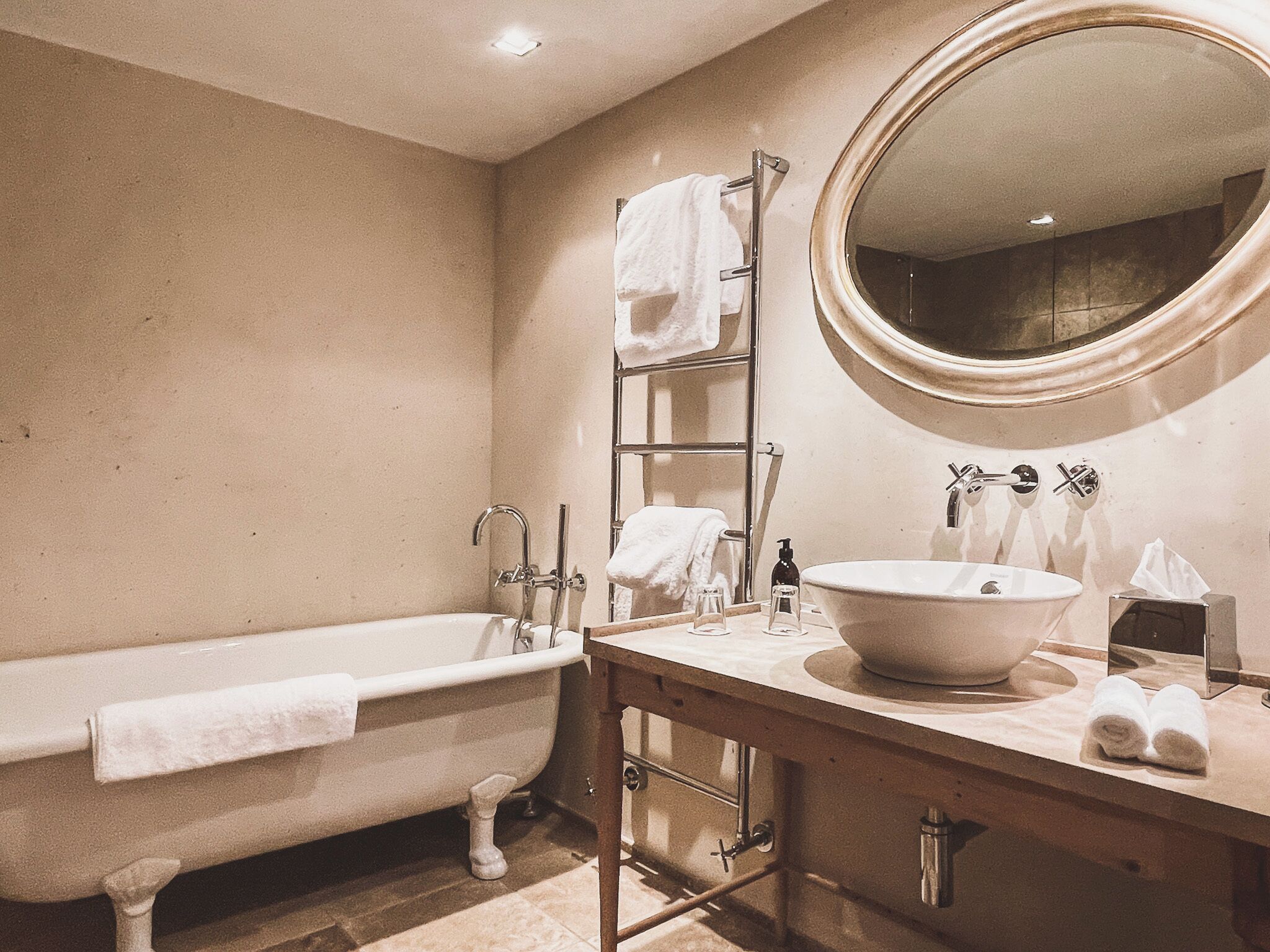 Un baño con una bañera, un espejo redondo, un lavabo con un recipiente amplio y un perchero para toallas.