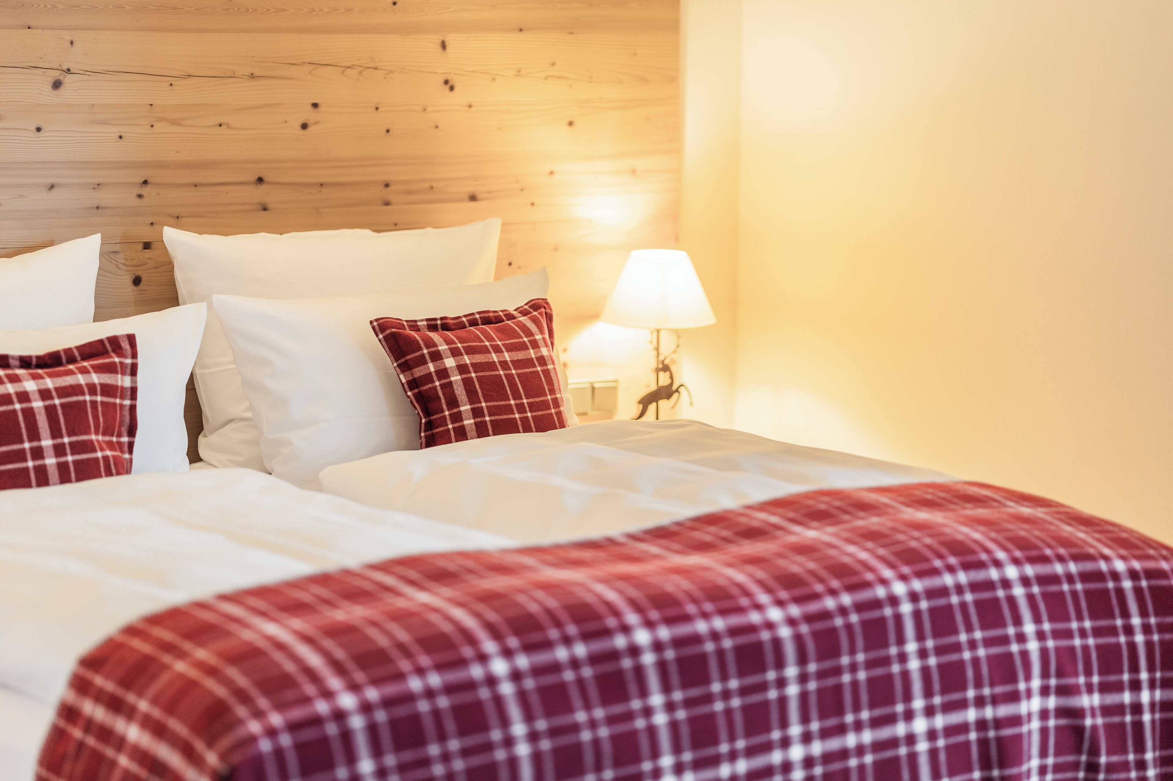 A bed with white and red plaid bedding, a wooden headboard, and a bedside lamp.