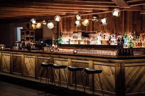 A bar with wooden paneling, hanging spherical lights, and stools.