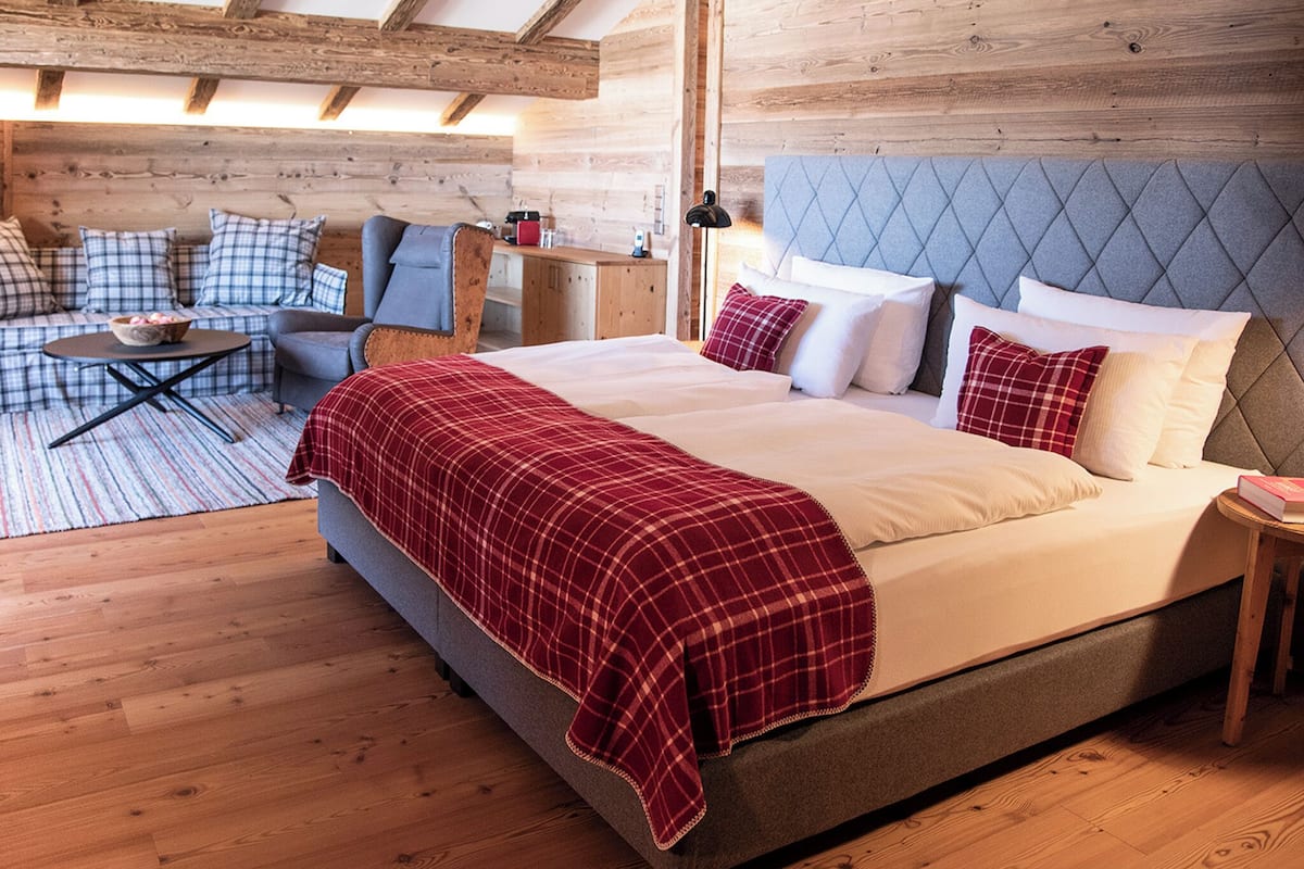 A bedroom with a large bed, a sofa, a small table, and a wooden ceiling.