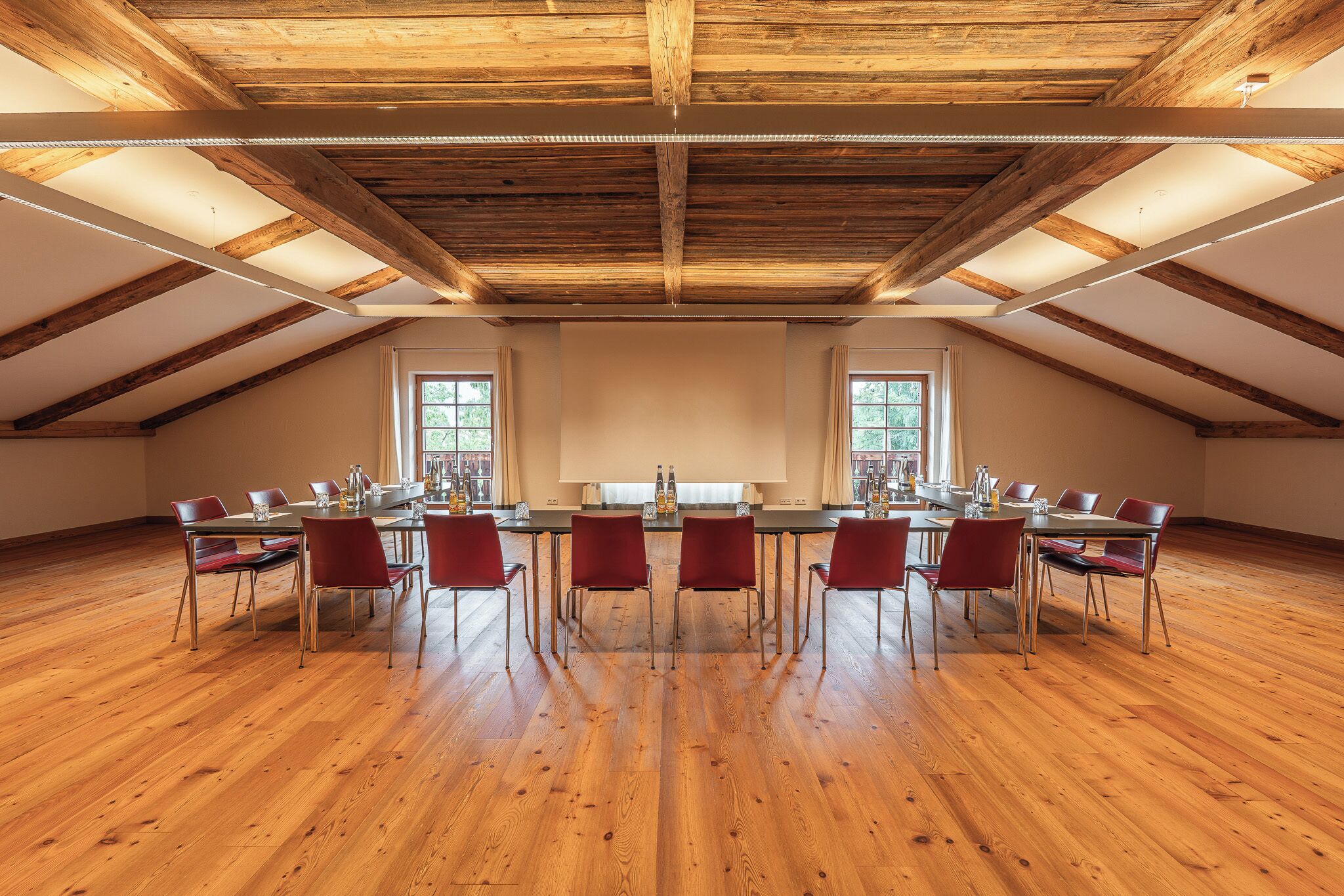 Una habitación amplia con un alto techo de madera, una mesa larga con sillas y ventanas grandes.