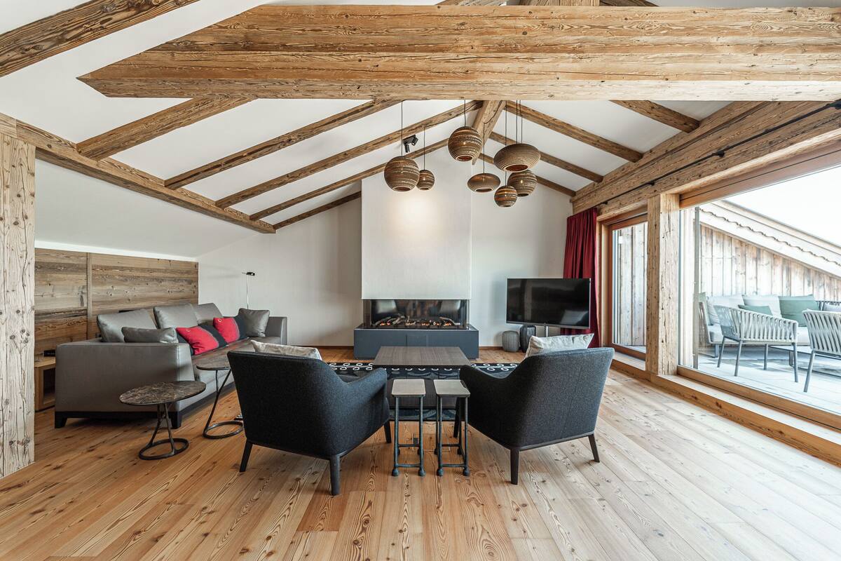 A spacious living area with a fireplace, wooden beams, and a large window.
