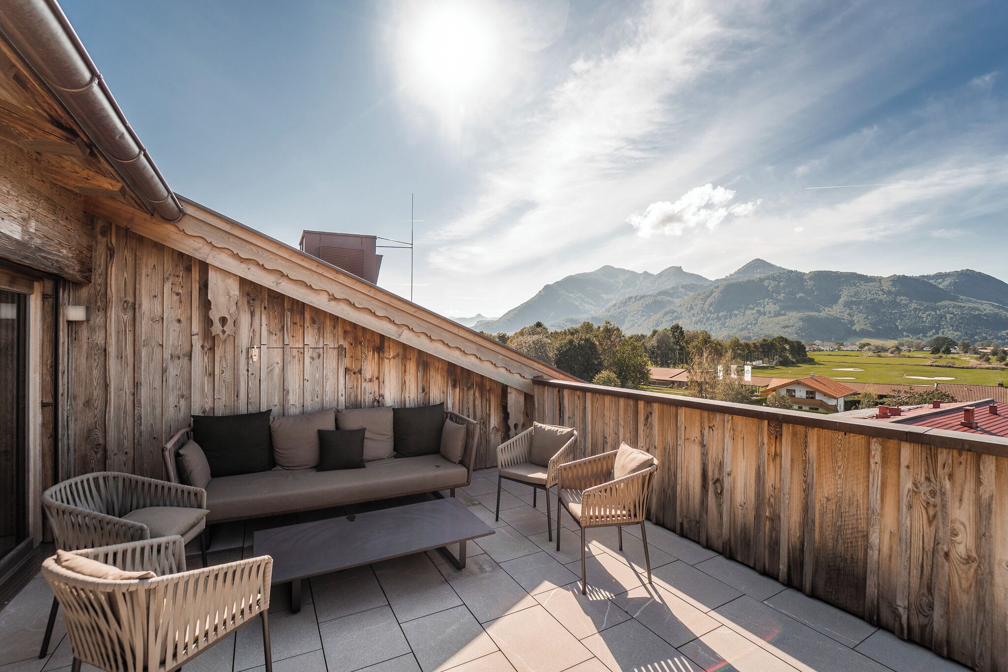 Un balcón de madera con sofá, sillas y vistas a montañas.