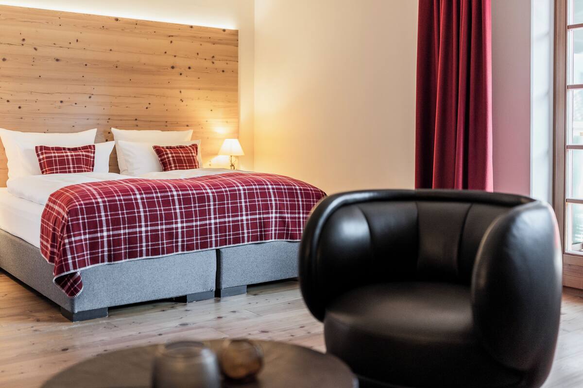 A hotel room with a bed, a chair, a lamp, and a window with curtains.