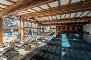 A spa area with wooden beams, large windows, and sun loungers. - Resort Das Achental (Grassau)