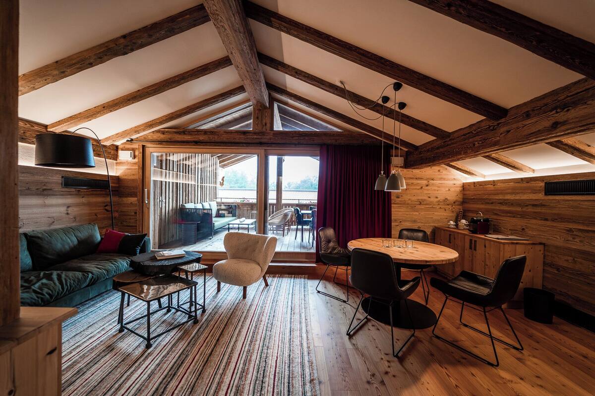 A cozy room with wooden beams, a sofa, a round table, and chairs.