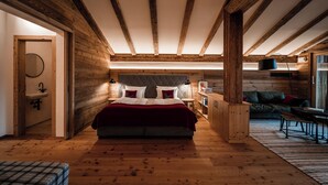 A bedroom with a wooden ceiling, a bed with pillows, a nightstand, a lamp, and a sofa. - Resort Das Achental (Grassau)