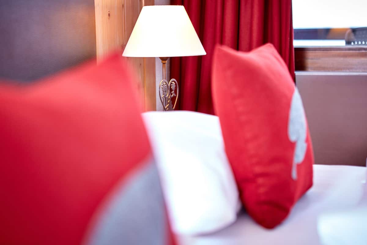 Een bed met rode en witte kussens, een bedlampje en een raam met rode gordijnen.