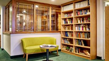 Un rincón de lectura con un sofá verde, una mesita con un libro abierto y una estantería llena de libros.