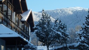 Un edificio cubierto de nieve con fachada de madera y vista a un bosque y montaña nevados al fondo.