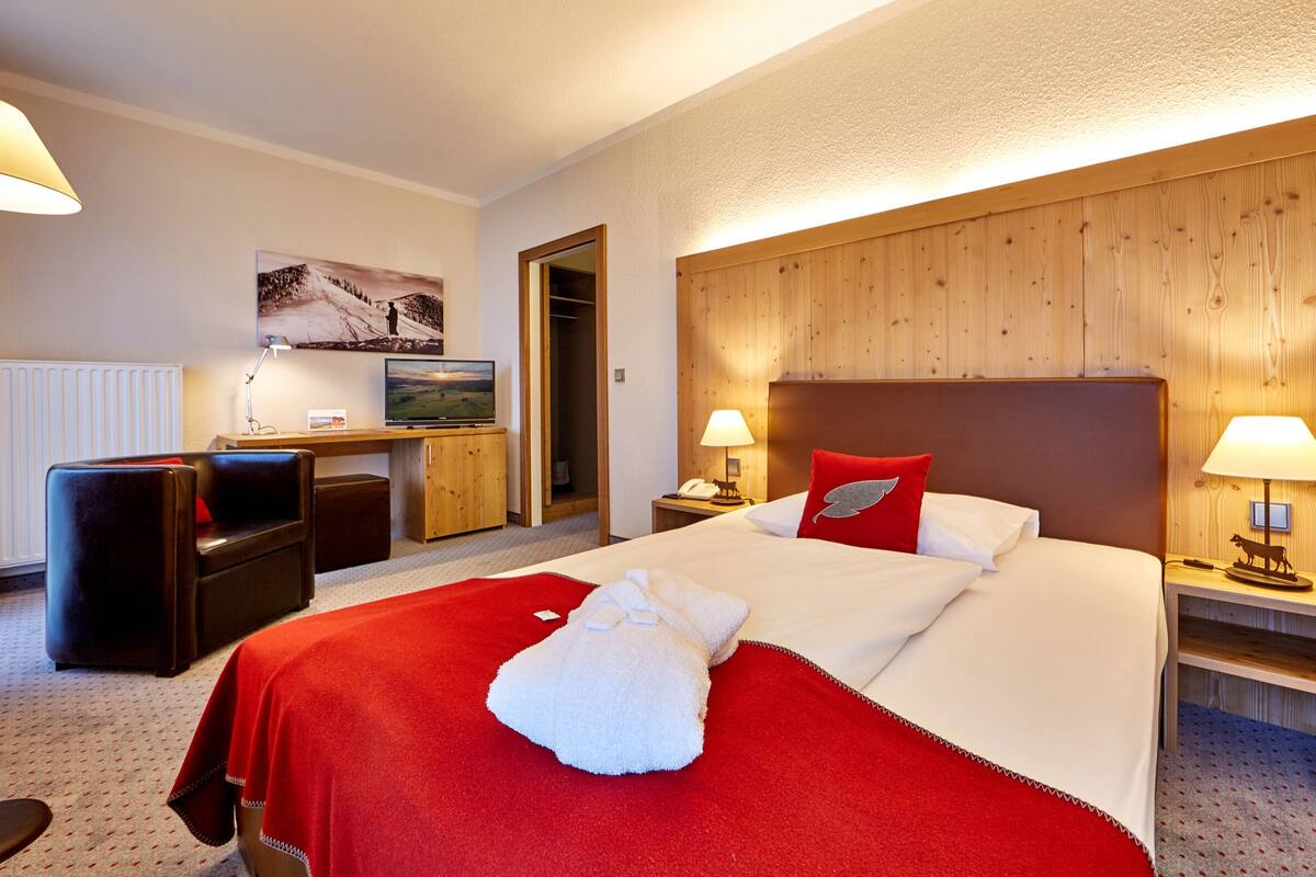 Hotelkamer met een groot bed, een bureau met een computer, een stoel, een televisie en een houten hoofdeinde.