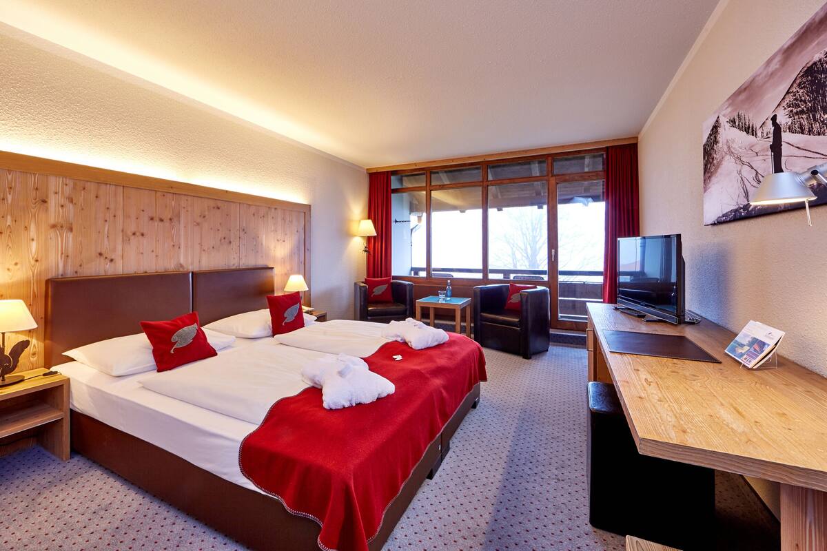 Een hotelkamer met een groot bed, een bureau, een stoel, een televisie en een raam met uitzicht op bomen.