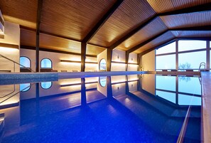 Una piscina interna moderna con travi in legno, ampie finestre e una vista aperta sul cielo.