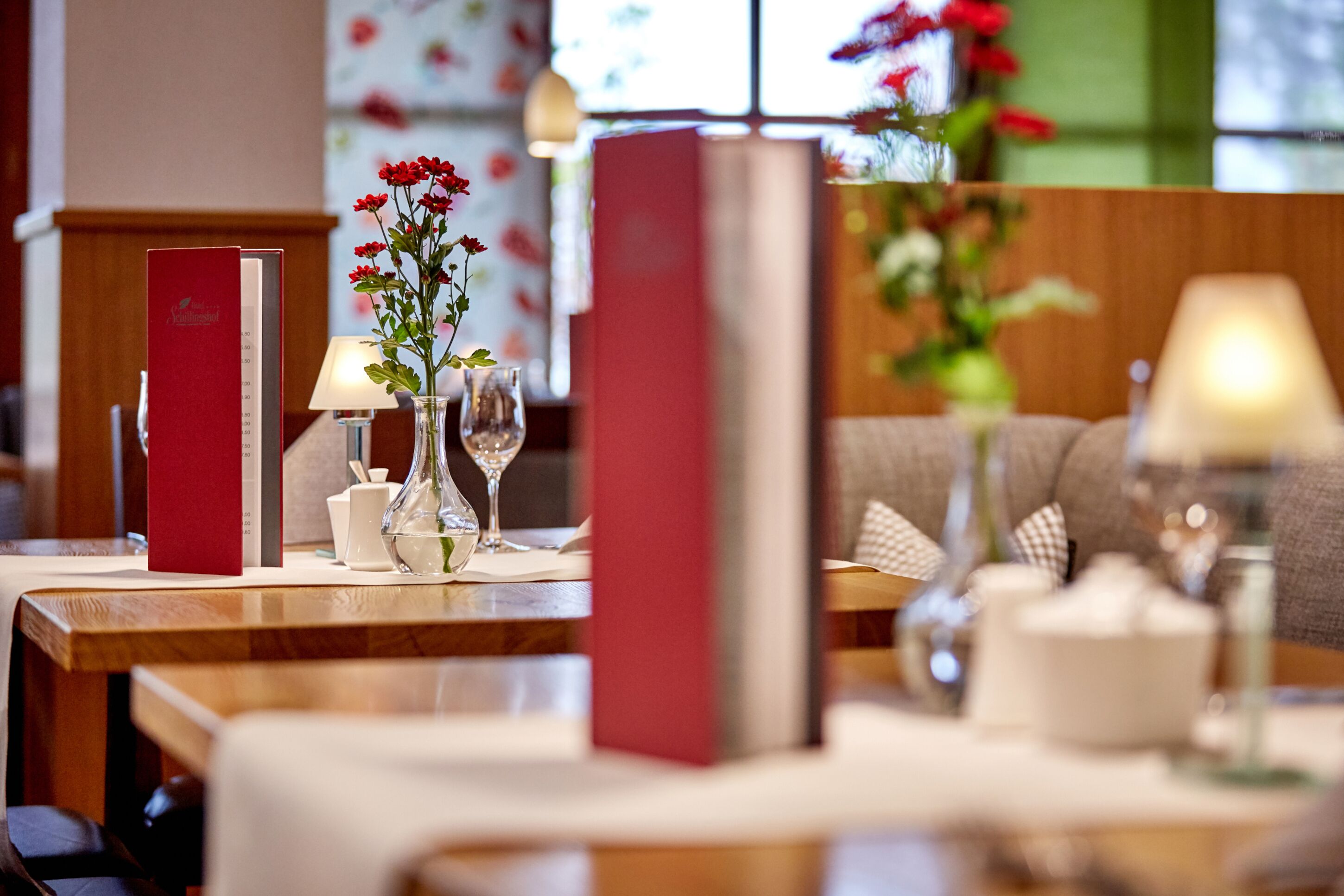 A dining area with a wooden table, red menu boards, a vase with red flowers, and a lamp.