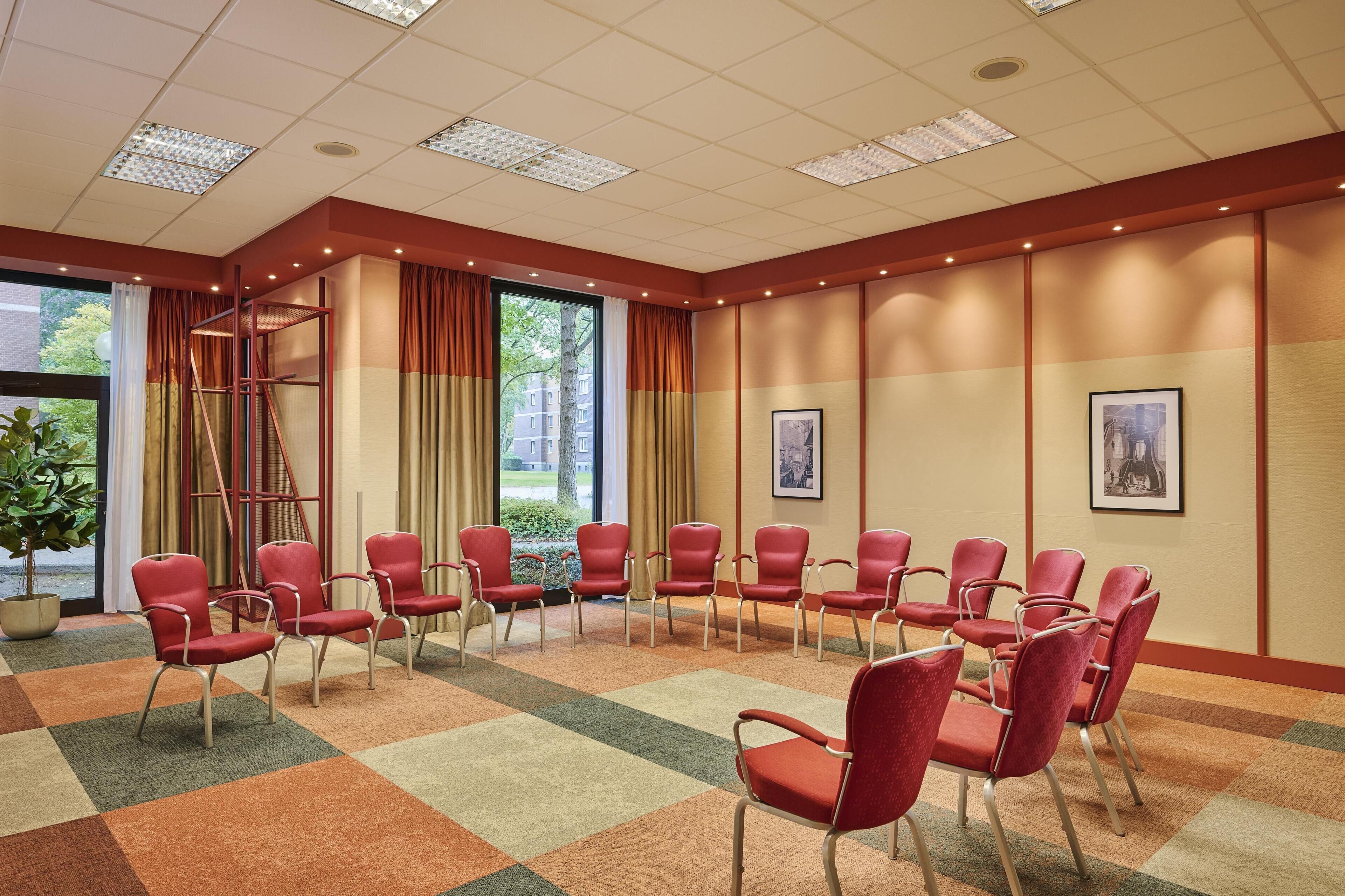 A conference room with red chairs arranged in a semi-circle, a ladder, and a large window with curtains.