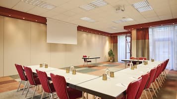 Une salle de conférence avec une longue table, des chaises rouges, un écran de projection et une grande fenêtre avec des rideaux.
