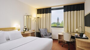 Habitación de hotel con cama, escritorio, silla y vista a un edificio por la ventana.