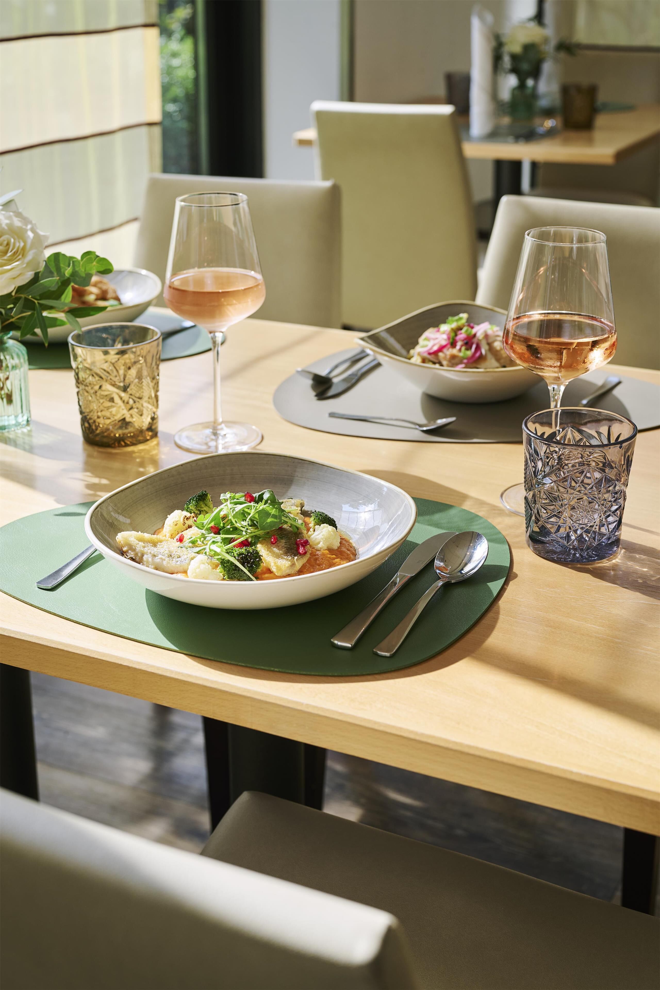 Una mesa de comedor con un tazón de comida, dos copas de vino y un vaso decorativo.