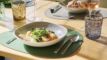 Una mesa de comedor con un tazón de comida, dos copas de vino y un vaso decorativo.