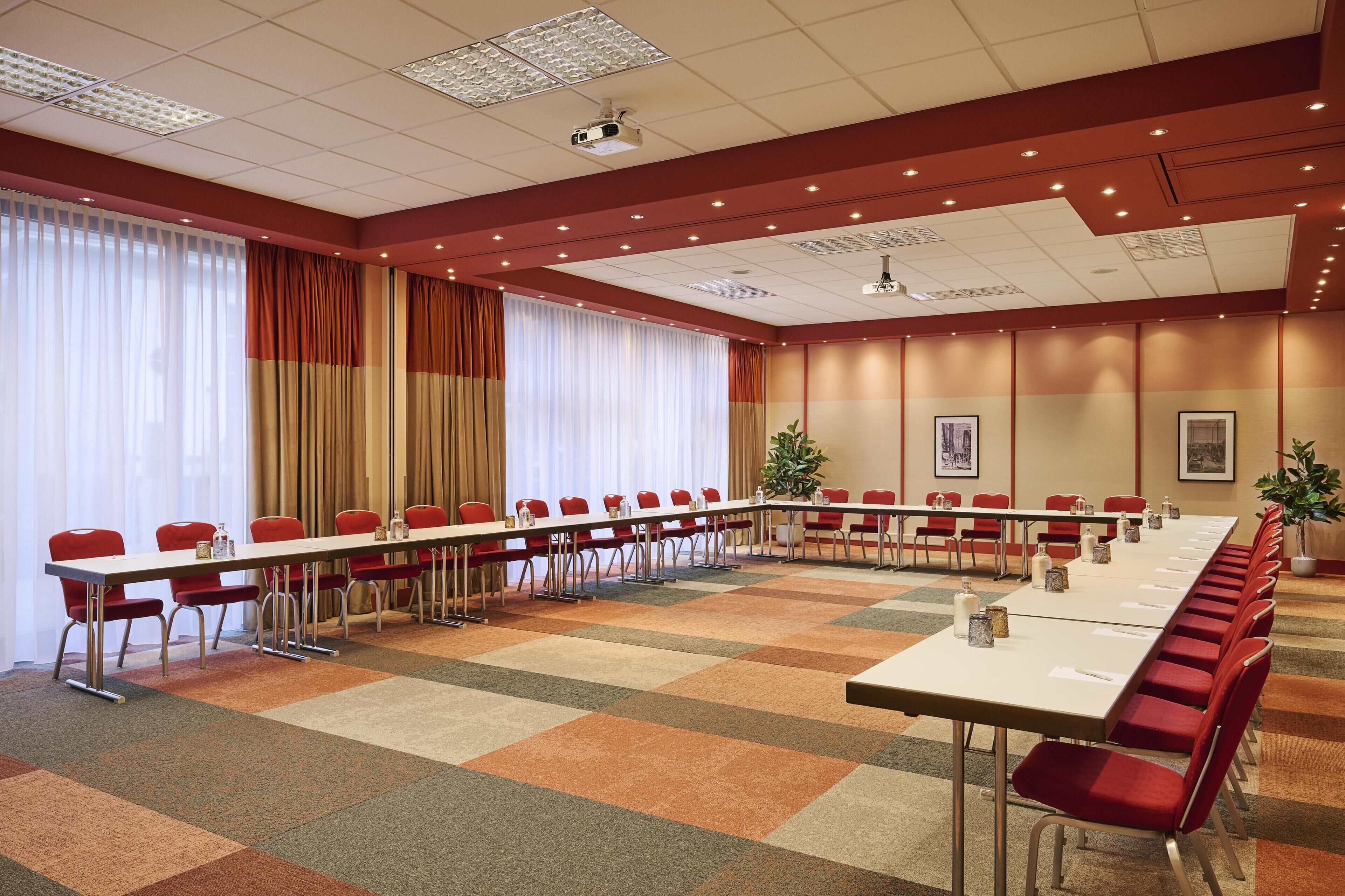 A conference room with a long table, red chairs, and a carpeted floor.