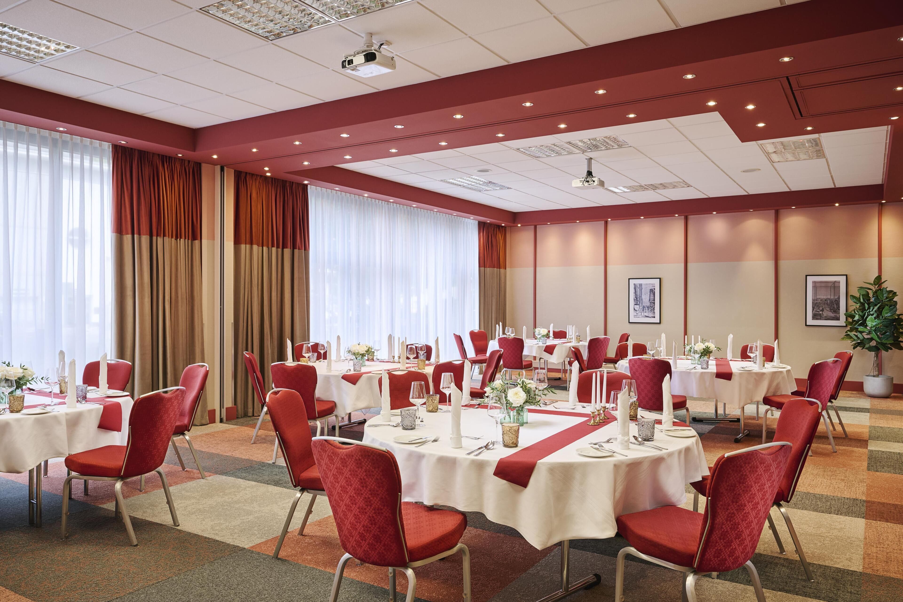 A conference room with multiple tables and chairs, equipped with white tablecloths and red chairs.