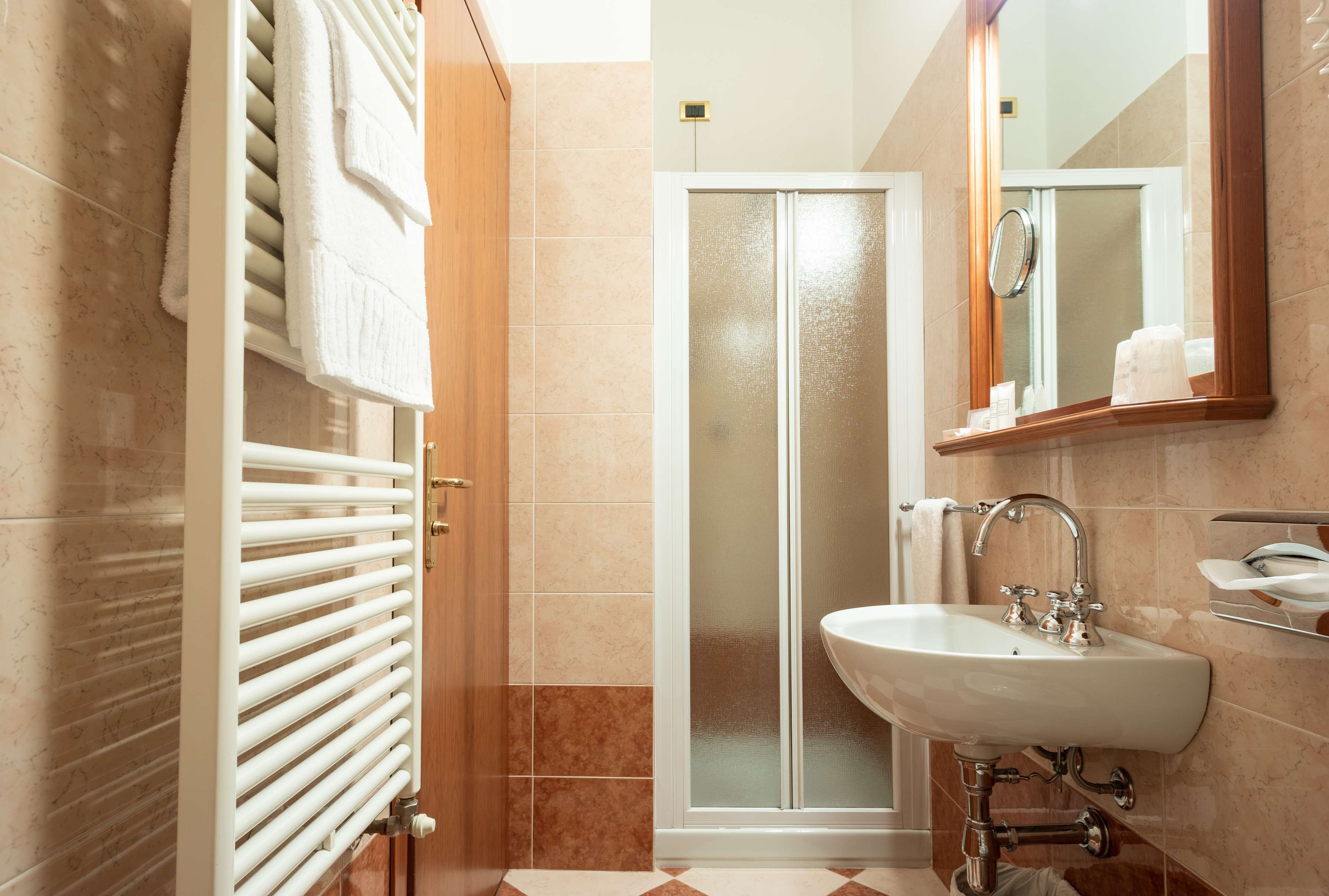 A bathroom with a white radiator, a glass shower enclosure, a sink with a mirror, and a towel rack.
