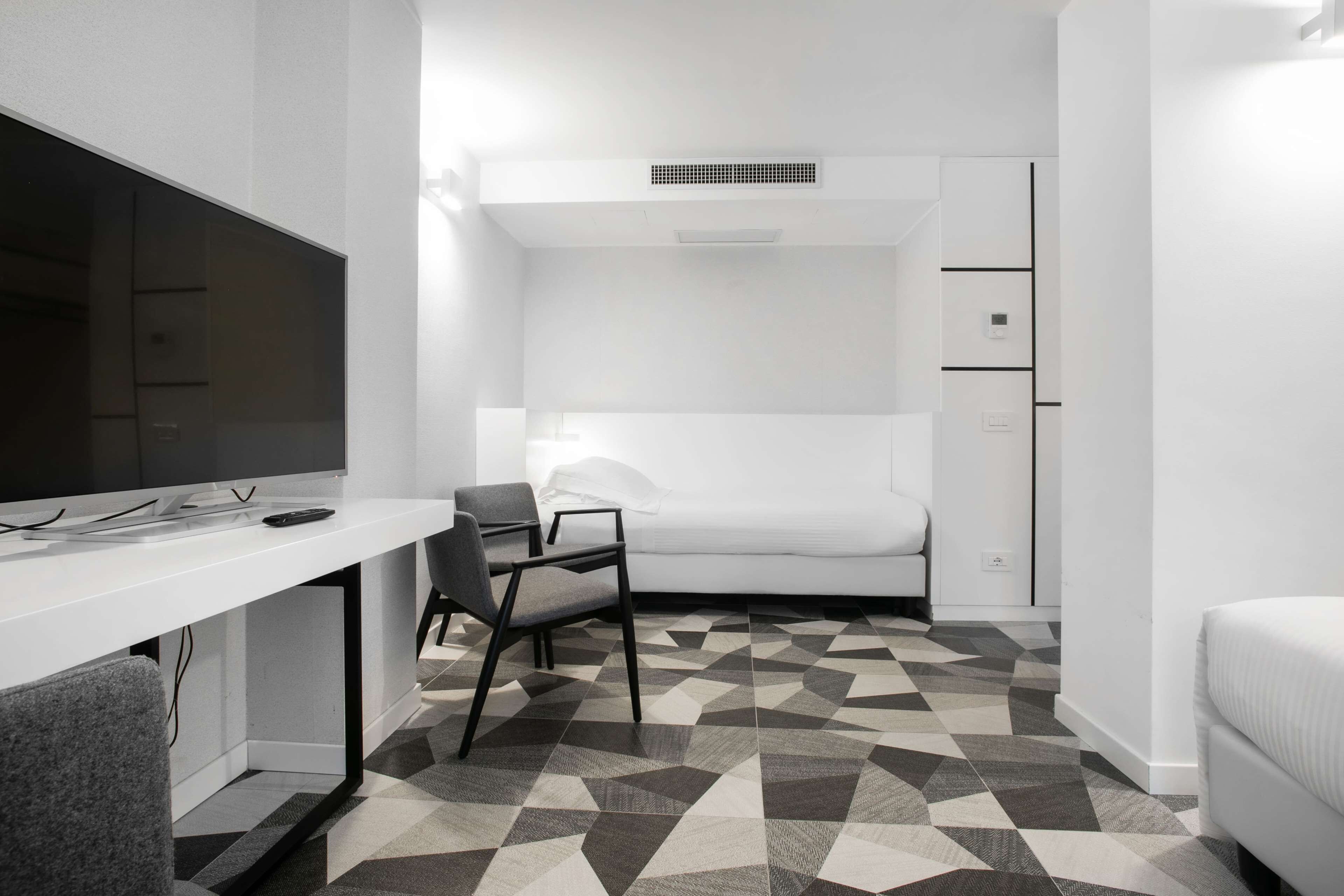 A modern, compact room with a white desk, a chair, a bed, and a wardrobe.