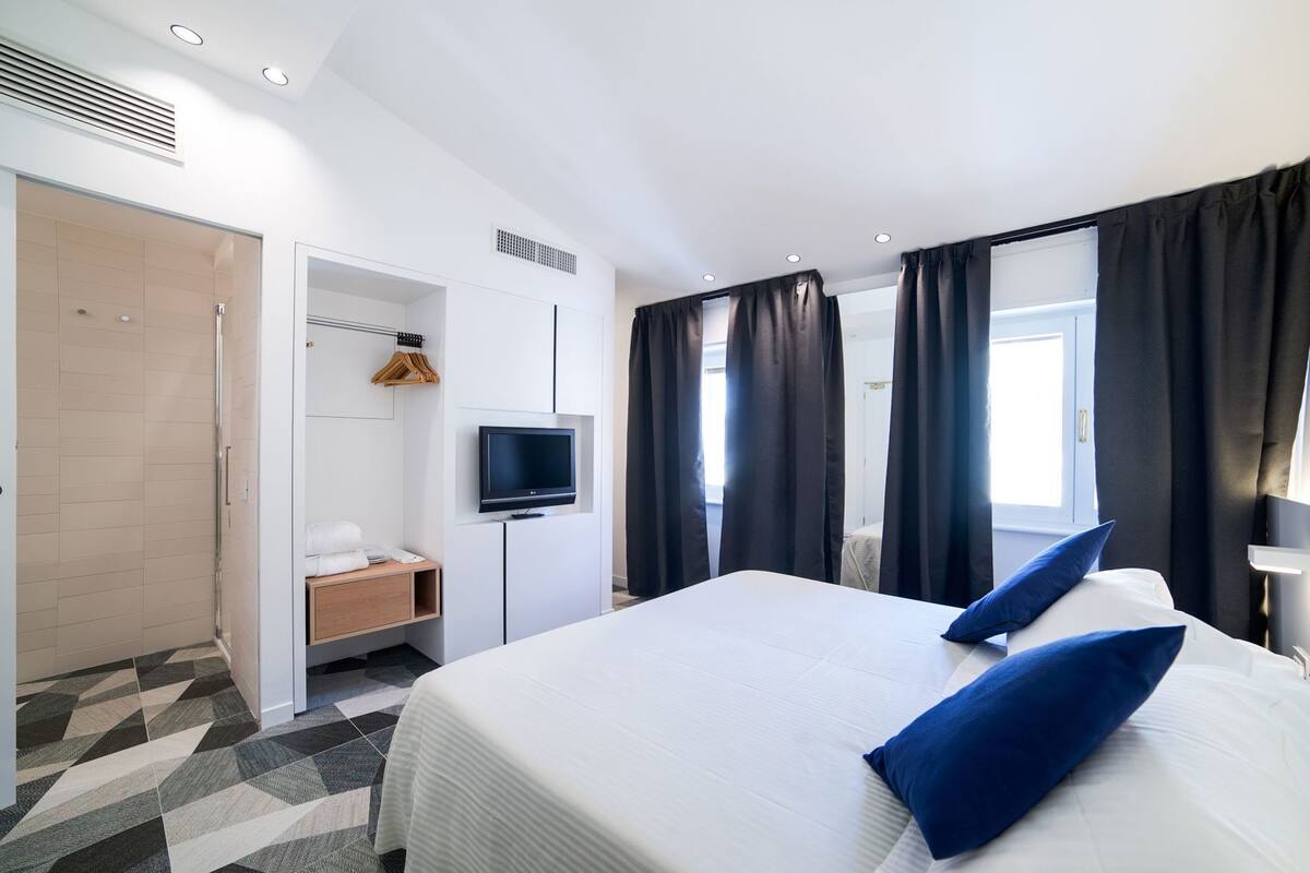A hotel room with a bed, a TV, a shower, and a desk.
