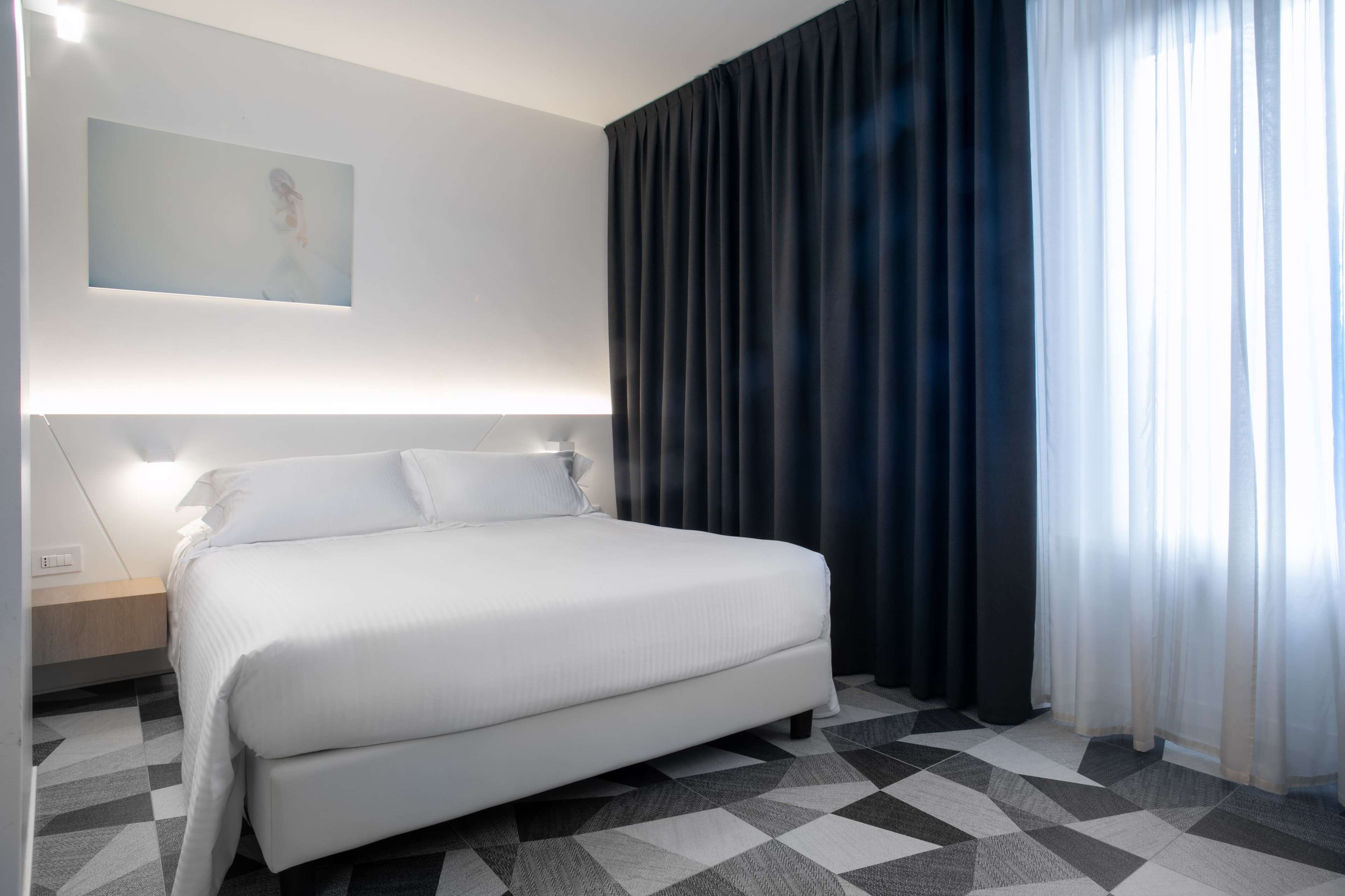 A modern hotel room with a large bed, a nightstand, and a painting on the wall.