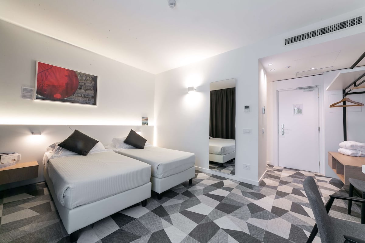 A hotel room with two beds, a mirror, a desk, and a chair.