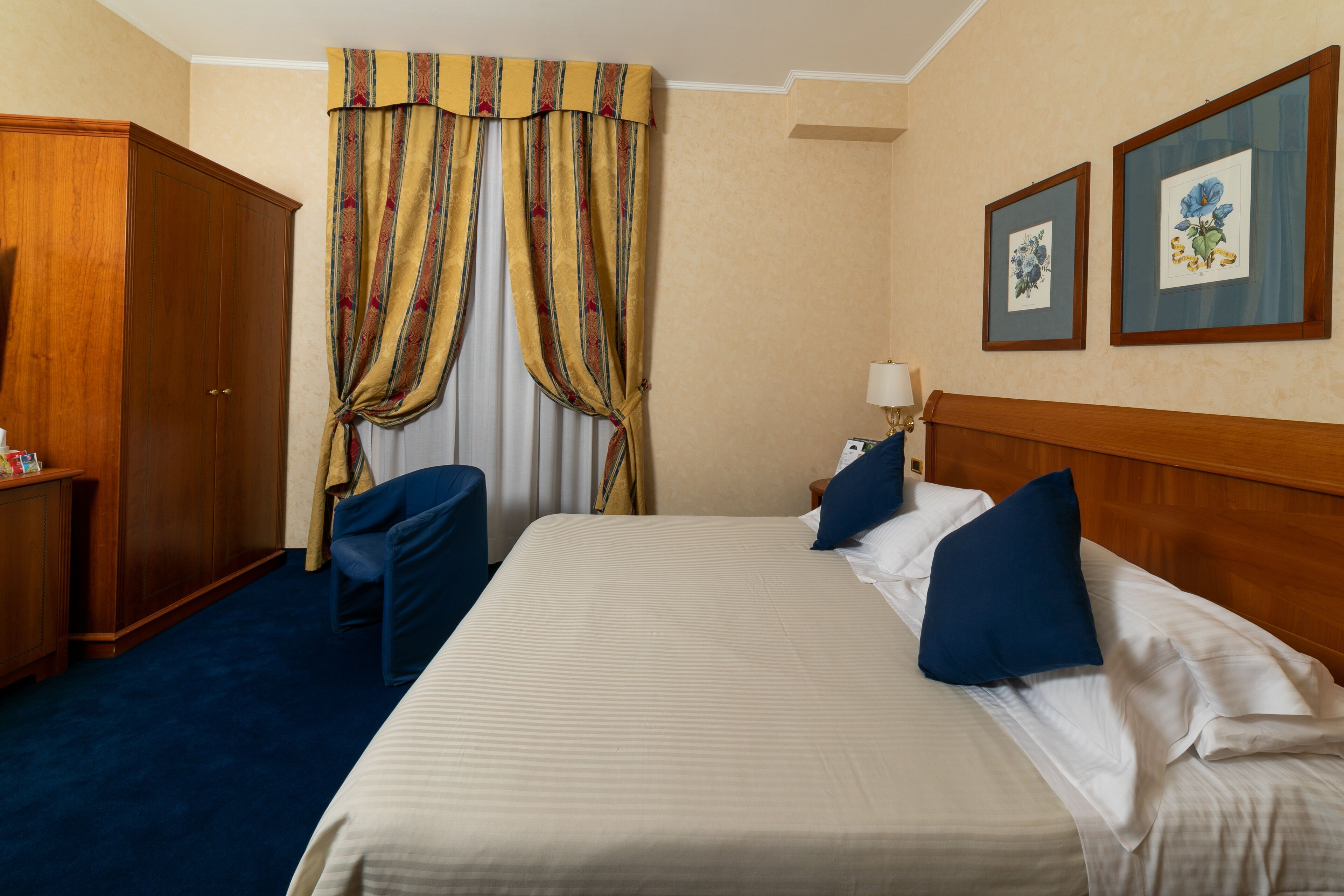 A hotel room with a large bed, a wooden wardrobe, a desk, and a chair.